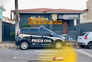 Viatura da Polícia Civil estacionada em frente à delegacia de Nepomuceno, com faixas de comunicação da DTTV sobre investigação de roubo em mercearia.